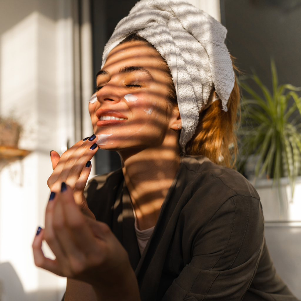 Femme recevant un soin du visage relaxant dans un salon de bien-être, allongée avec une serviette sur la tête et un professionnel appliquant un masque facial.